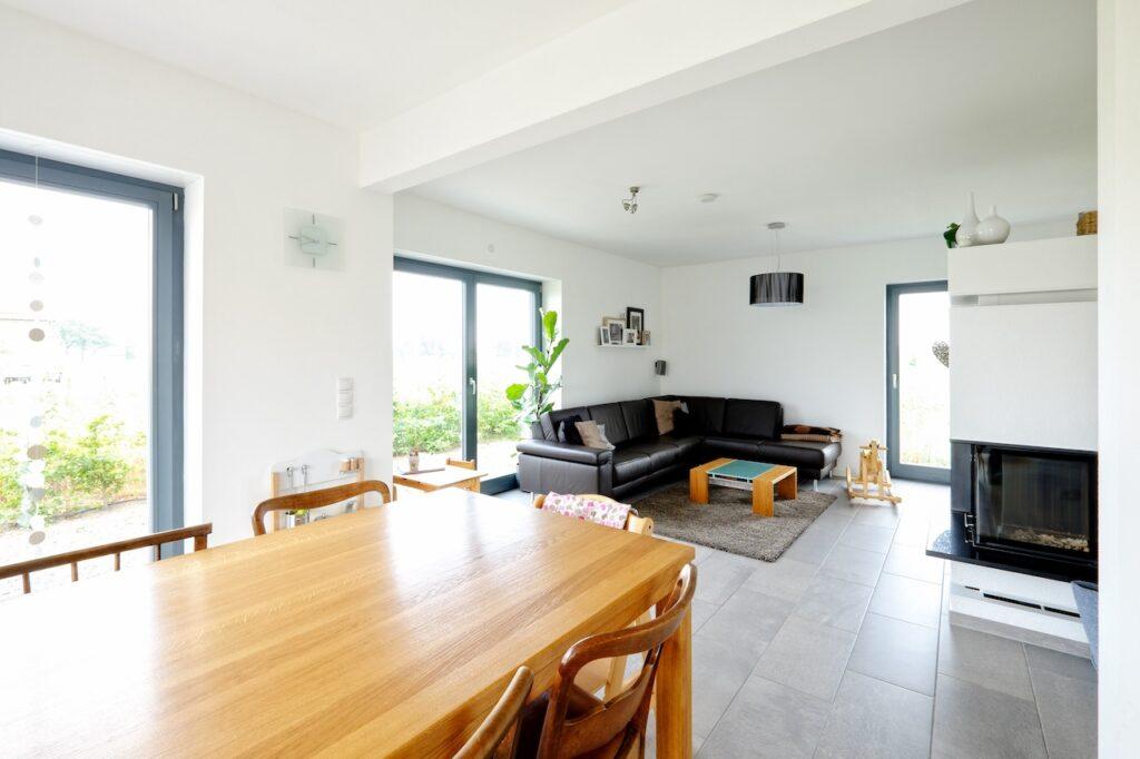 Heller Wohn-Essbereich mit einem großen Massivholztisch, eleganten Holzstühlen und einer gemütlichen Sitzecke mit dunklem Sofa. Der Raum kombiniert moderne Architektur mit natürlicher Wärme.