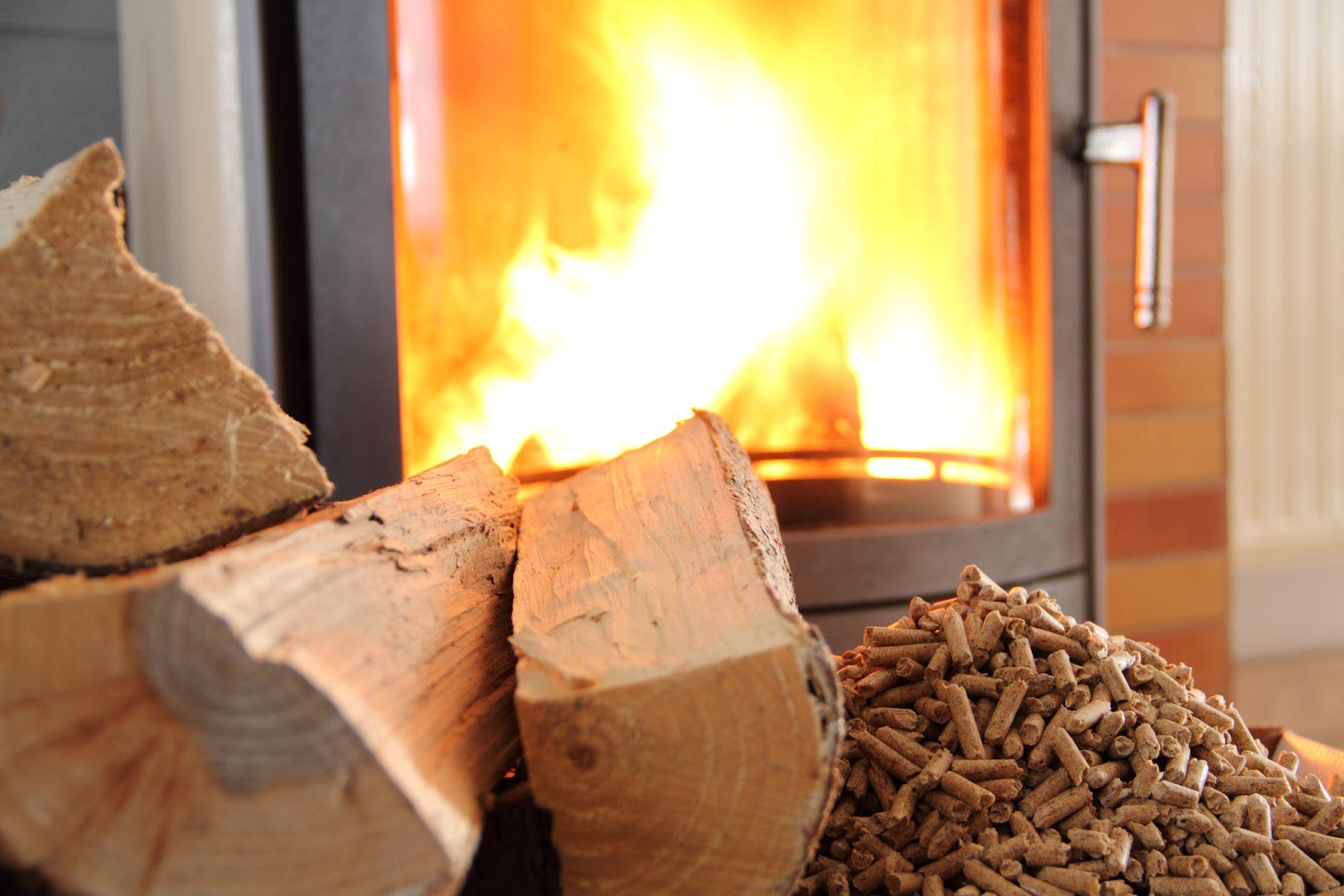 Scheitholz und Holzpellets vor einem brennenden Specksteinofen im Nahaufnahme